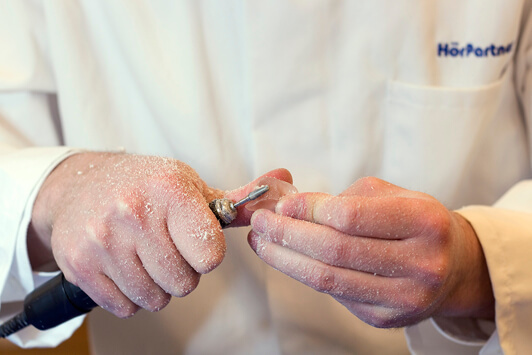 Ein Akustiker passt individuell ein Hörgerät mit speziellem Werkzeug in der Werkstatt an.